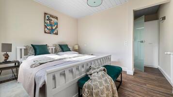 Ein Schlafzimmer mit Bett, Nachttischen, einer Lampe, einem Gemälde und einer Tür zu einem anderen Raum.