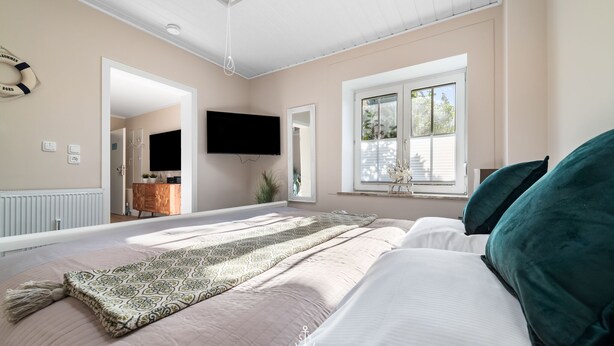 A bedroom with a large bed, a TV mounted on the wall, and a window with a view of the outside. - Ferienwohnung Deck 3 Büsum (Büsum)