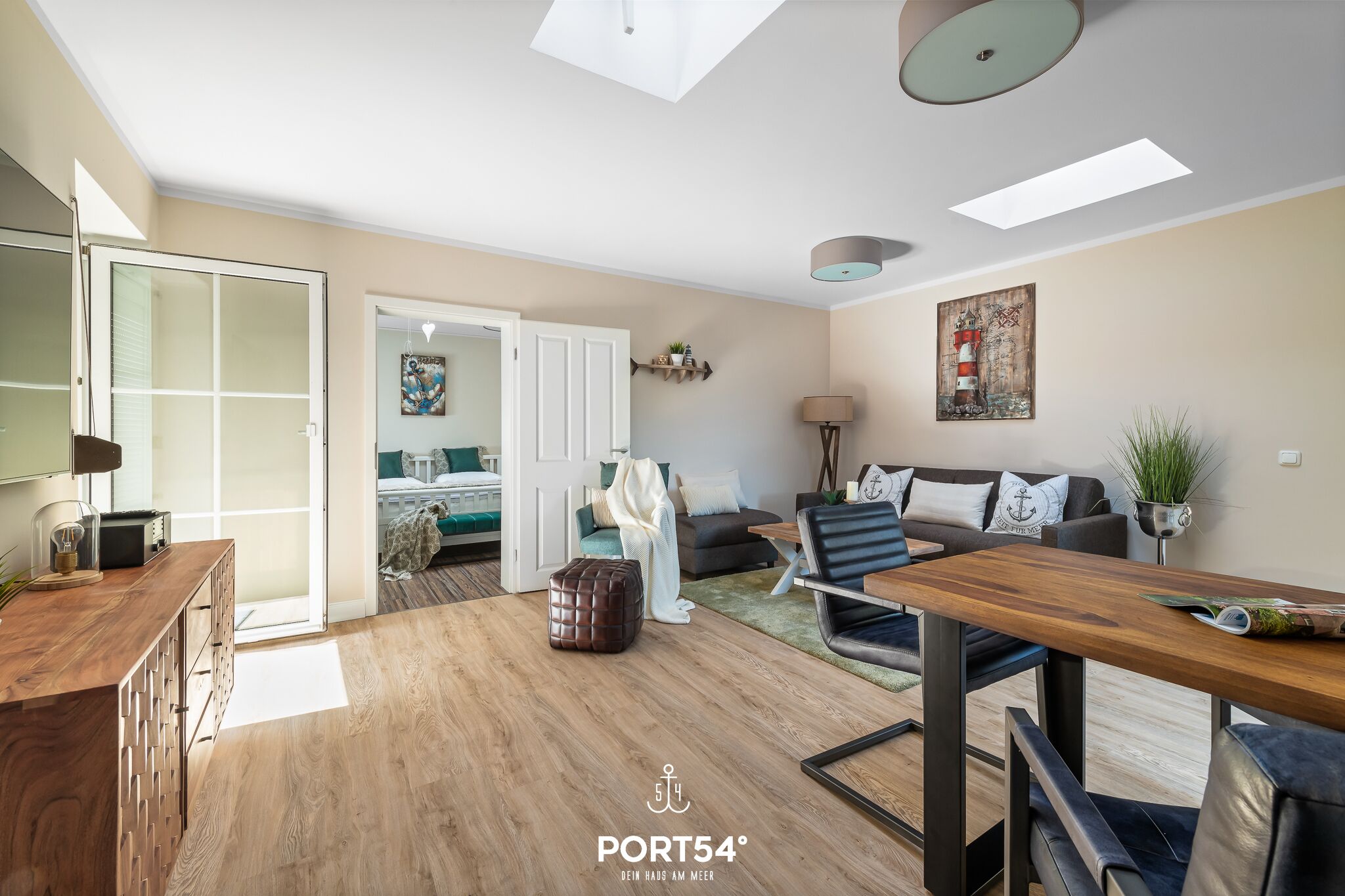Ein modernes Wohnzimmer mit Holzboden, einem Esstisch und einem Sofa. Eine Tür führt in einen weiteren Raum.
