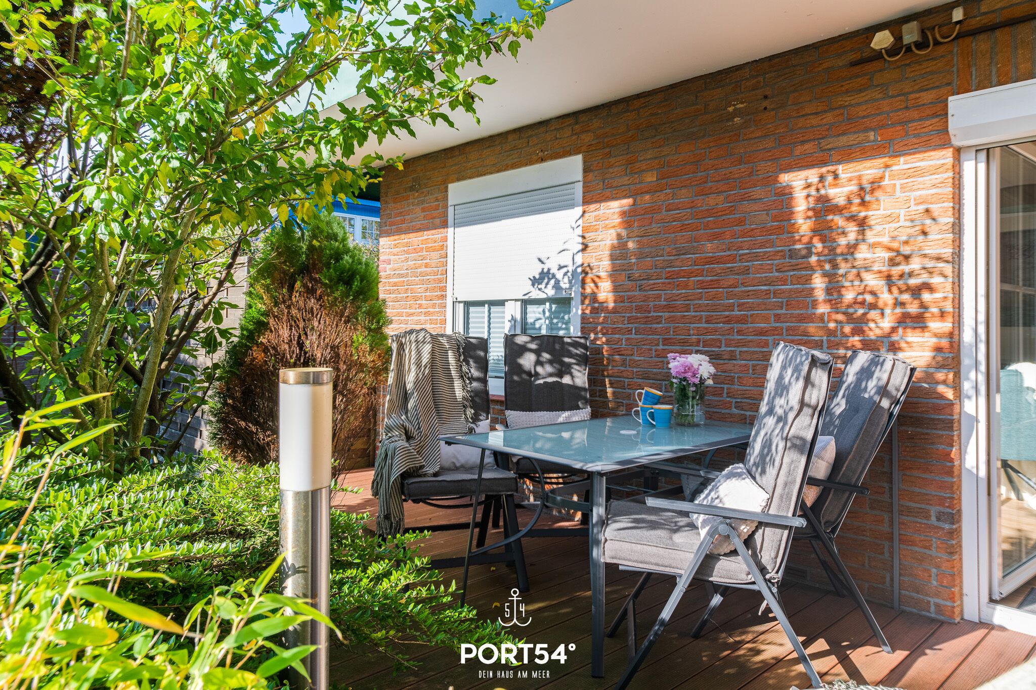 A patio with a table and chairs, a brick wall, and a sliding glass door.
