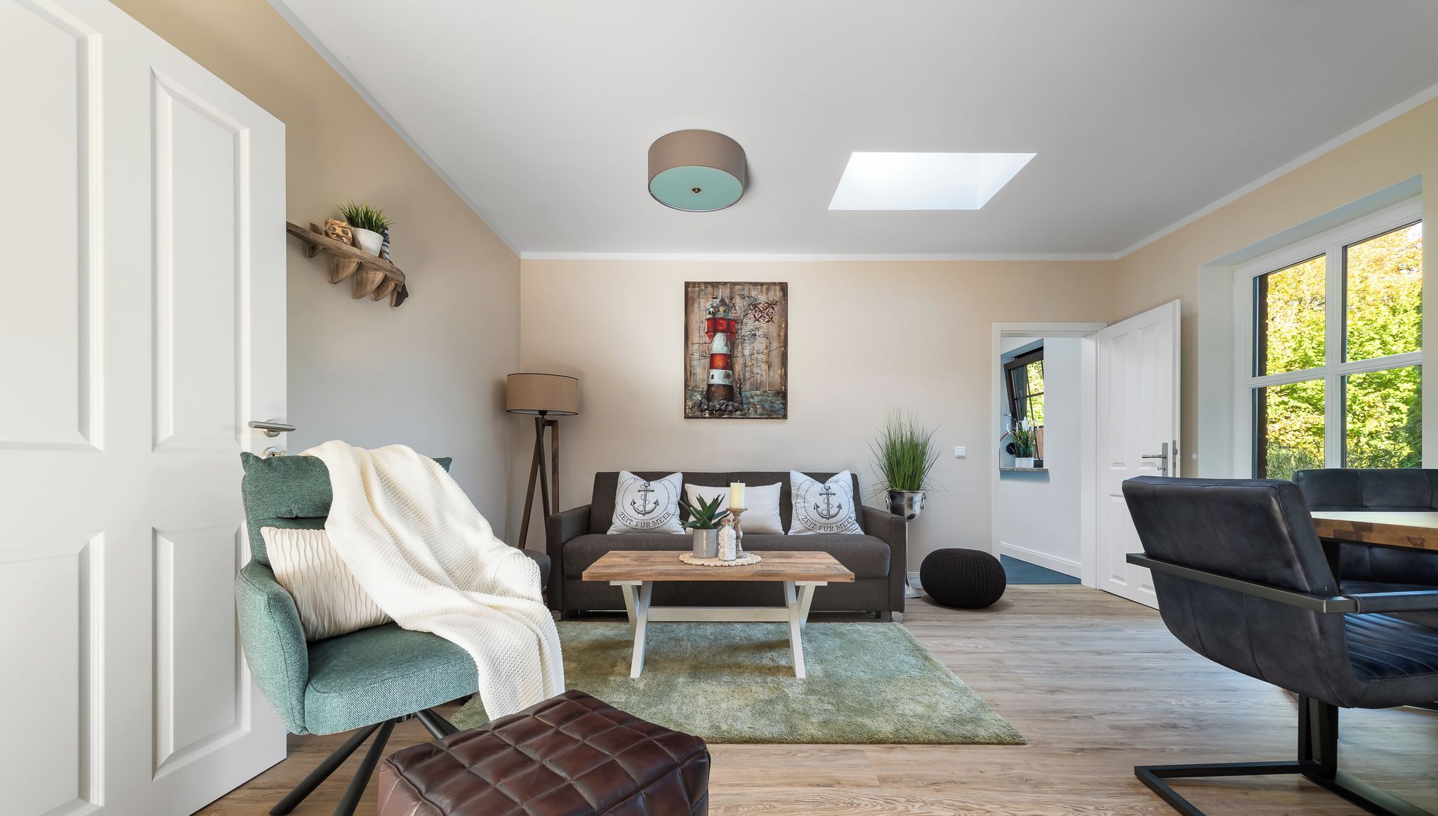 Ein modernes Wohnzimmer mit einer Couch, einem Couchtisch und einem Lederhocker. Eine Lampe, ein Gemälde an der Wand und ein Fenster sorgen für natürliches Licht.