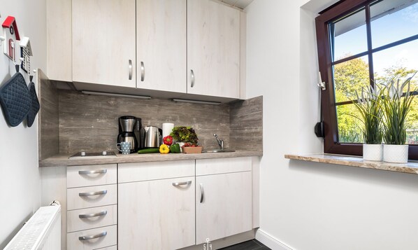 A modern kitchen with wooden cabinets, a built-in stove, and a window with a view of trees. - Ferienwohnung Deck 3 Büsum (Büsum)