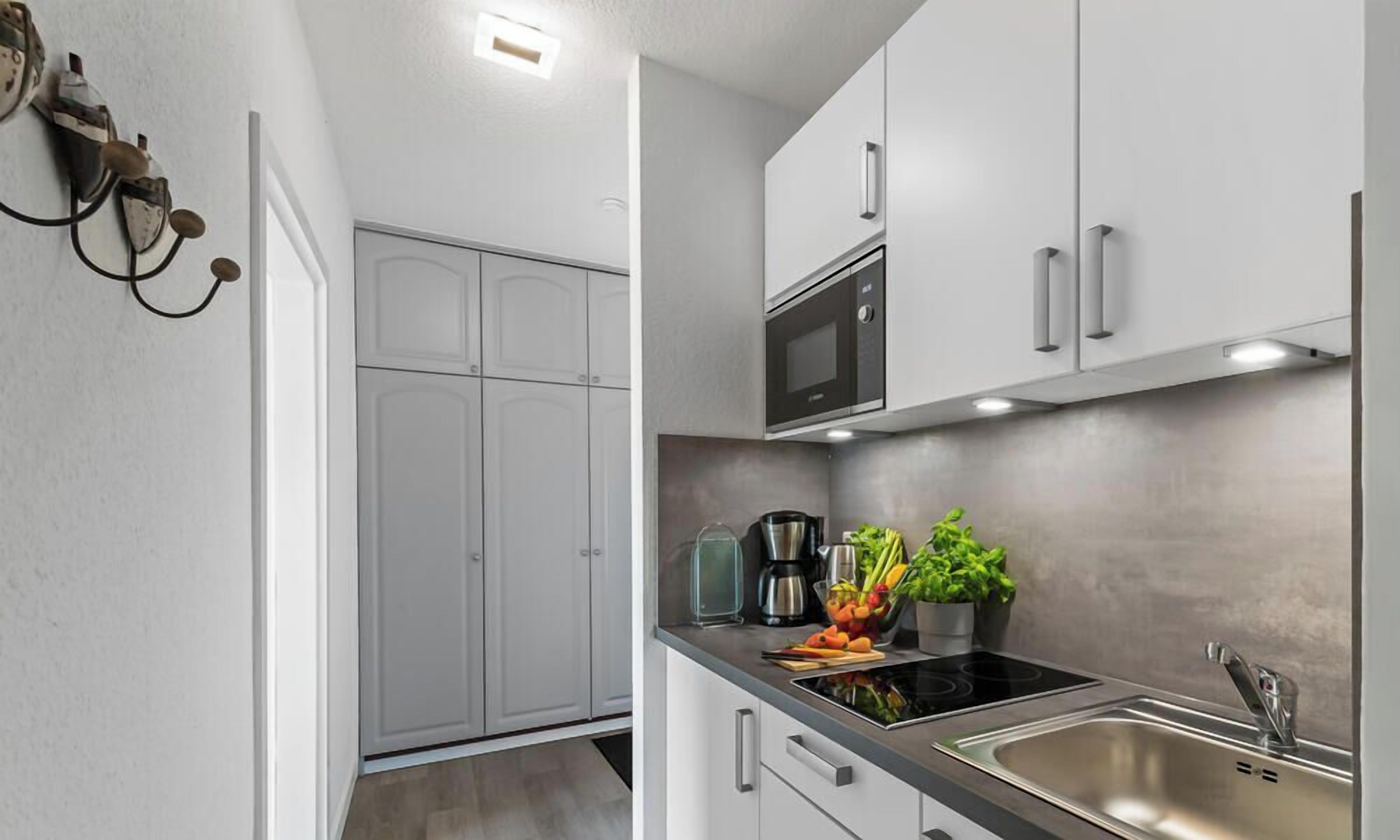 Una cocina moderna con gabinetes blancos, un lavamanos de acero inoxidable y un microondas integrado.