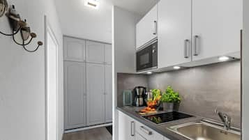 Una cocina moderna con gabinetes blancos, un lavamanos de acero inoxidable y un microondas integrado.