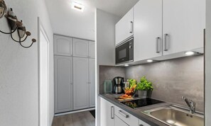A modern kitchen with white cabinets, a microwave, a sink, and a countertop with a coffee maker and fresh vegetables.