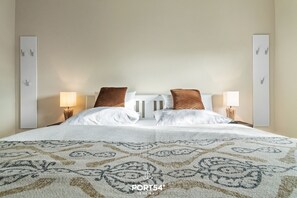 A neatly made bed with a patterned bedspread, two pillows, and two bedside lamps.