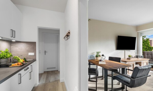 Una cocina moderna con armarios blancos, encimera de madera y zona de comedor con mesa de madera y sillas negras.