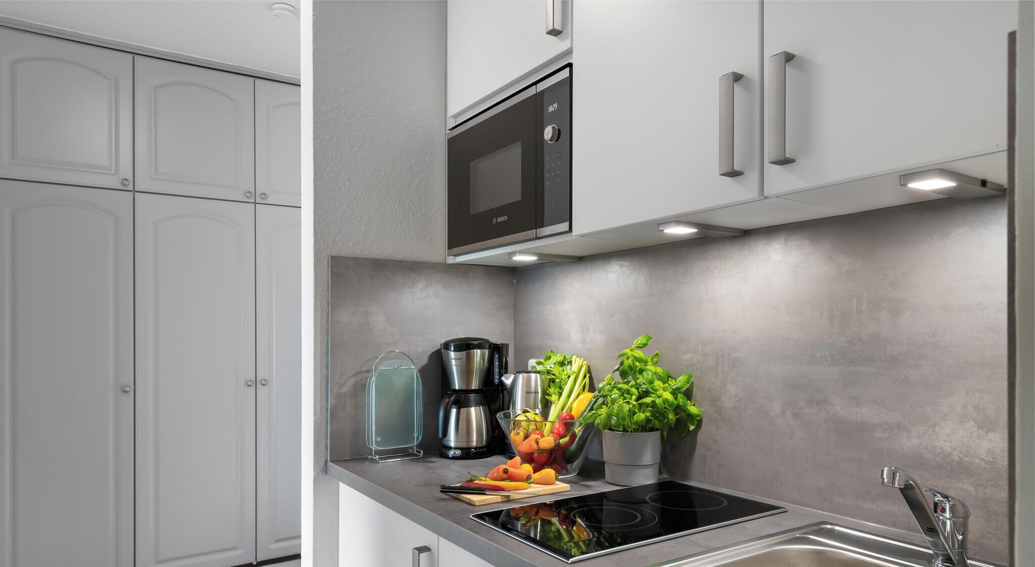 Une cuisine moderne dotée d’un four à micro-ondes encastré, d’un évier en acier inoxydable et d’une plaque de cuisson à induction noire.