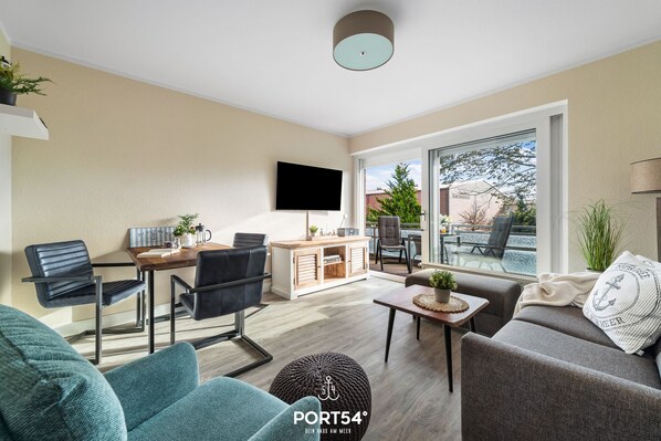 A modern living room with a dining area, a sofa, a coffee table, and a TV mounted on the wall.