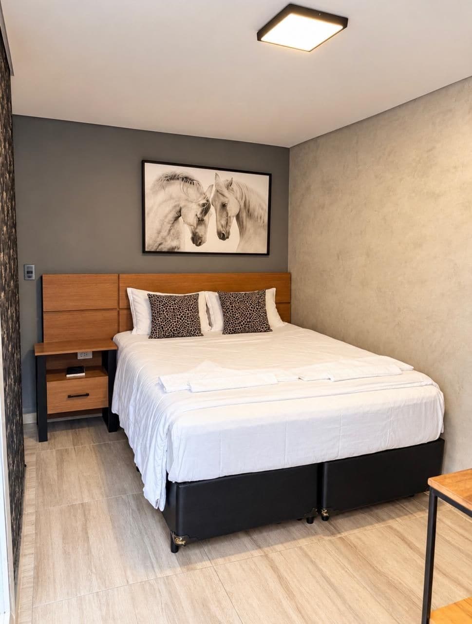 Quarto moderno com cama grande, mesa de cabeceira, cabeceira de madeira e obra de arte na parede.