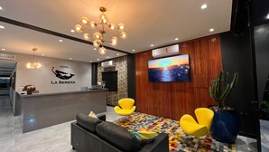A modern hotel lobby with a reception desk, a large TV screen, a wooden accent wall, and a colorful patterned rug. - Hotel la serena (Sao Sebastiao)