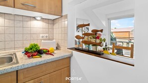Eine Küche mit Holzschränken, einer Arbeitsplatte mit frischem Obst und Gemüse, und einem Fenster mit Blick auf einen Balkon.