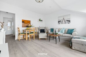 Ein modernes Wohnzimmer mit einer Couch, Sesseln, einem Esstisch und einer Küche im Hintergrund.