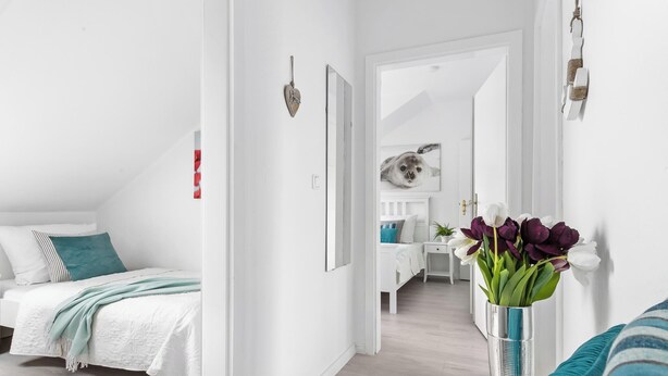 Ein modernes Schlafzimmer mit Bett, Nachttisch, Spiegel und einer Vase mit Blumen.