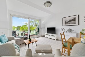 Ein modernes Wohnzimmer mit einer Couch, einem Esstisch, einem Fernseher und einem Balkon mit Gartenmöbeln.