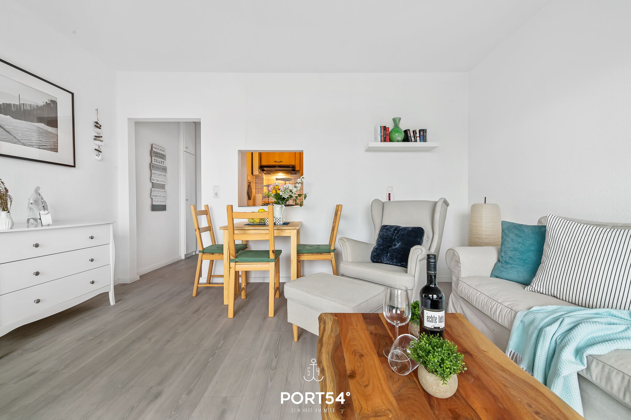 Ein modernes Wohnzimmer mit Essbereich, einer Couch, einem Couchtisch mit Flasche und Gläsern sowie einem Bücherregal.