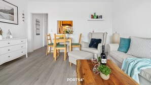 Ein modernes Wohnzimmer mit Essbereich, einer Couch, einem Couchtisch mit Flasche und Gläsern sowie einem Bücherregal.