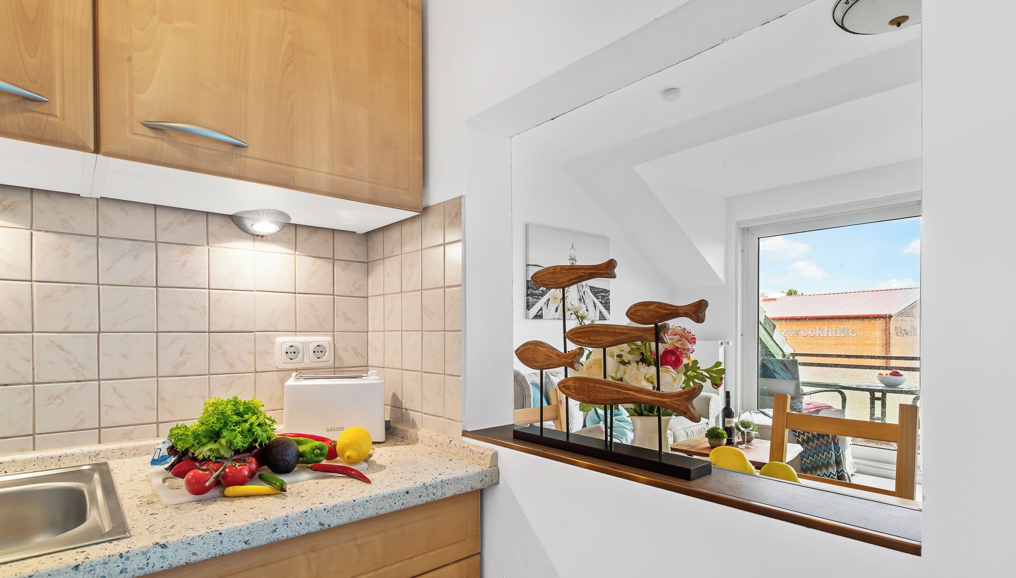 Una cocina con armarios de madera, una encimera con productos frescos y una ventana con vistas a un balcón.