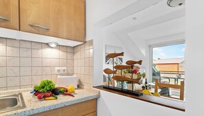 A kitchen with wooden cabinets, a countertop with fresh produce, and a window overlooking a balcony.