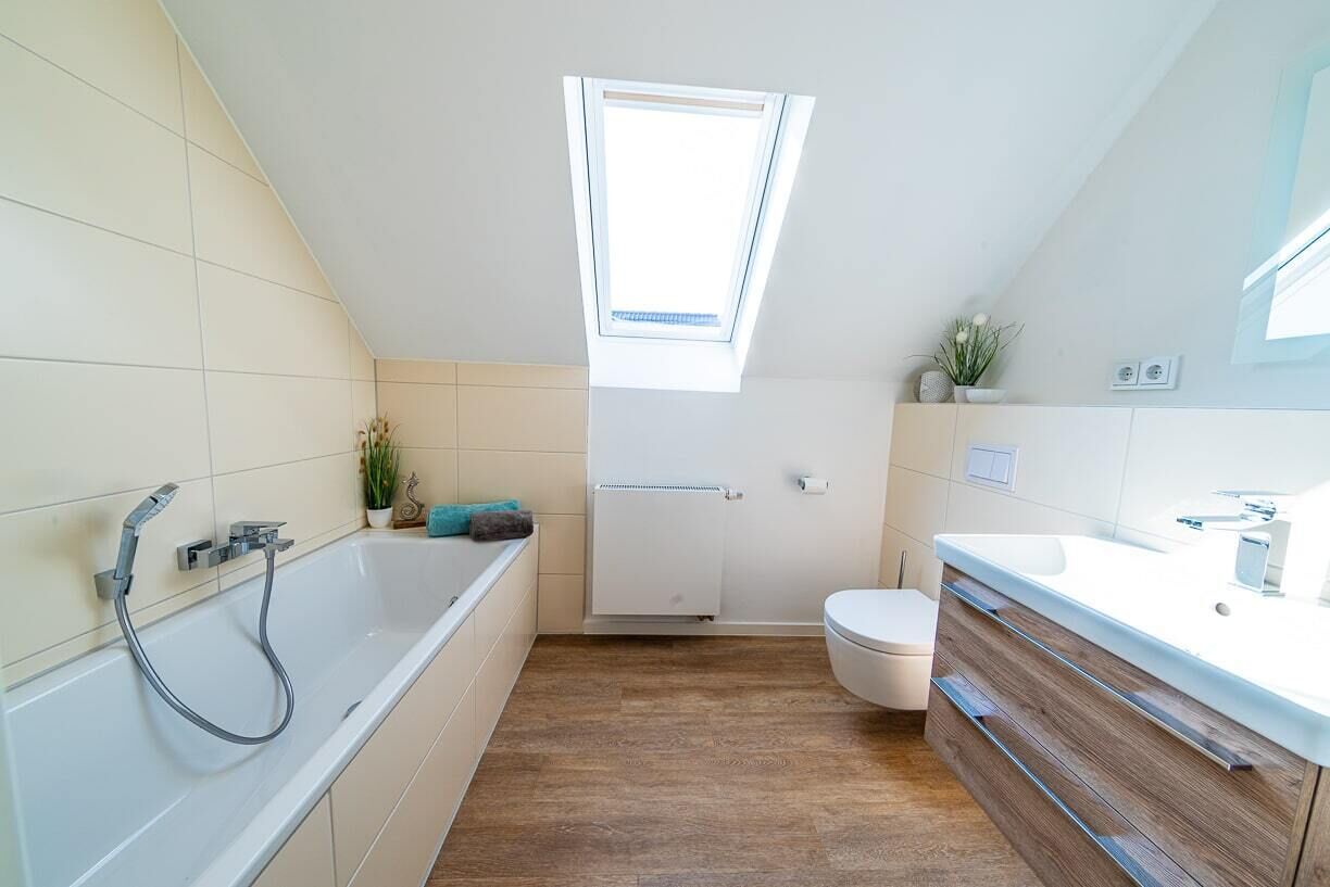 Et moderne badeværelse med ovenlys, badekar med brusehoved, toilet og et vaskeskab med spejl.