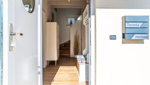 Een hal met een houten vloer, een witte deur en een trap die naar een andere kamer leidt. Er hangen borden aan de muur die verschillende secties aangeven.