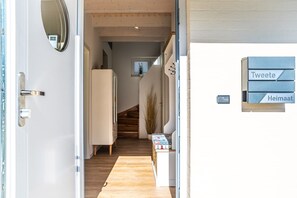 A hallway with a wooden floor, a white door, and a staircase leading to another room. There are signs on the wall indicating different sections. - Ferienhaus Tweete Heimaat Büsum (Büsum)