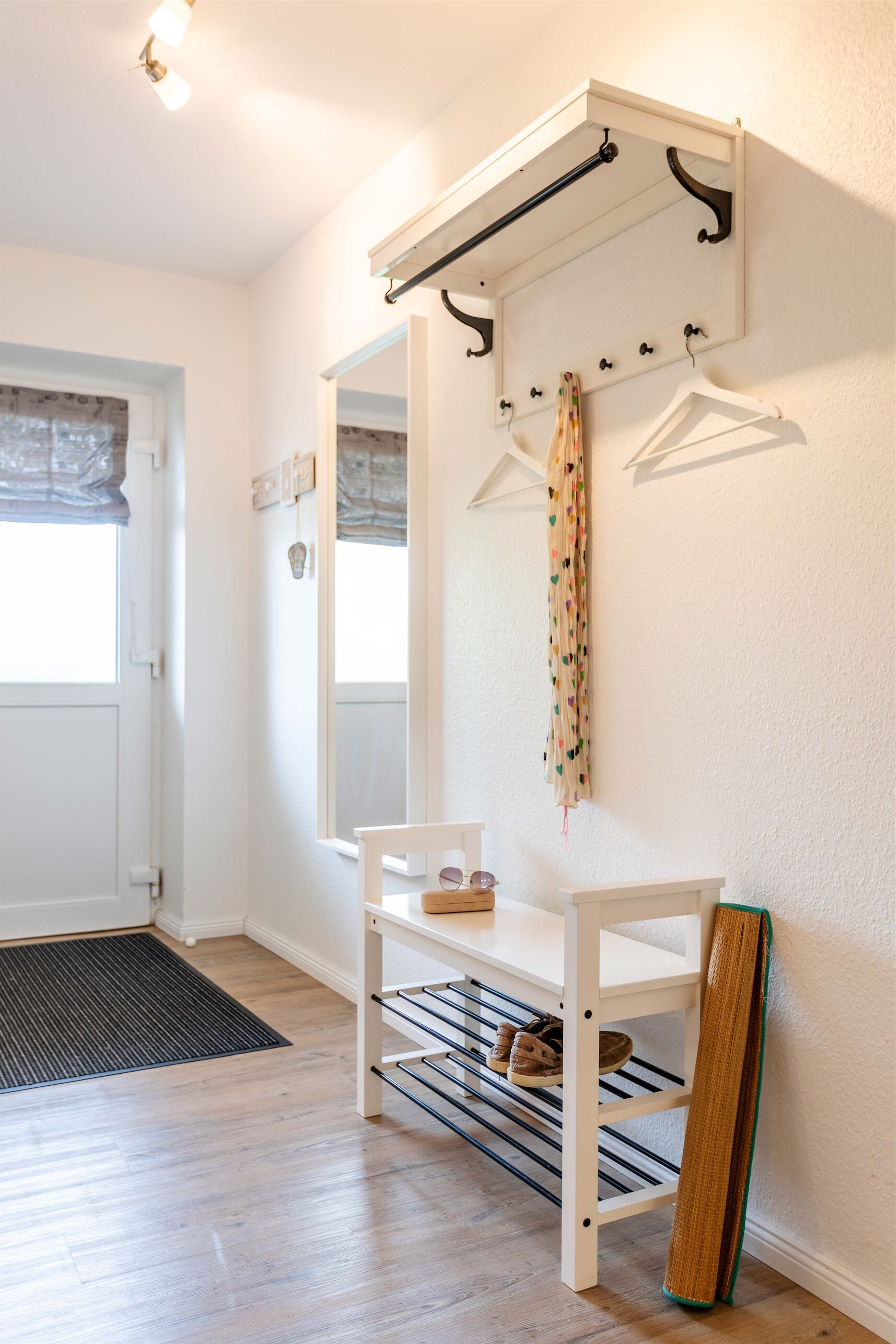 Une pièce comprenant un banc blanc, un miroir, un porte-manteau et un meuble à chaussures.