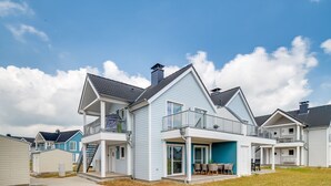 Et moderne hus med to etager, en balkon, en overdækket terrasse og en synlig trappe.