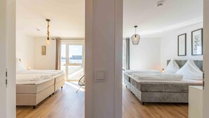 A modern bedroom with a large bed, a smaller bed, and a seating area with a view of the outdoors. - Gode Tied - Fireplace, Infrared Sauna, Bathtub, Shower, Balcony, Parking Space (Olpenitz)