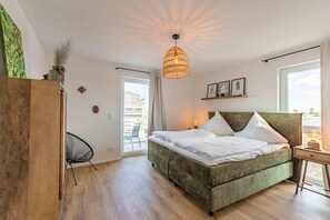 Une chambre avec un lit recouvert d’un tissu vert, un luminaire suspendu, une chaise et une vue sur l’extérieur.