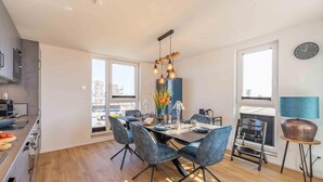 A modern kitchen with a built-in oven, a dining area with a large table and chairs, and a view of the city through large windows. - Gode Tied - Fireplace, Infrared Sauna, Bathtub, Shower, Balcony, Parking Space (Olpenitz)