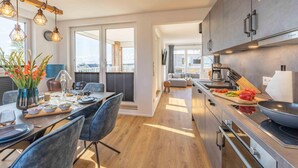 A modern kitchen with a dining area, wooden flooring, and a view of the city. - Gode Tied - Fireplace, Infrared Sauna, Bathtub, Shower, Balcony, Parking Space (Olpenitz)
