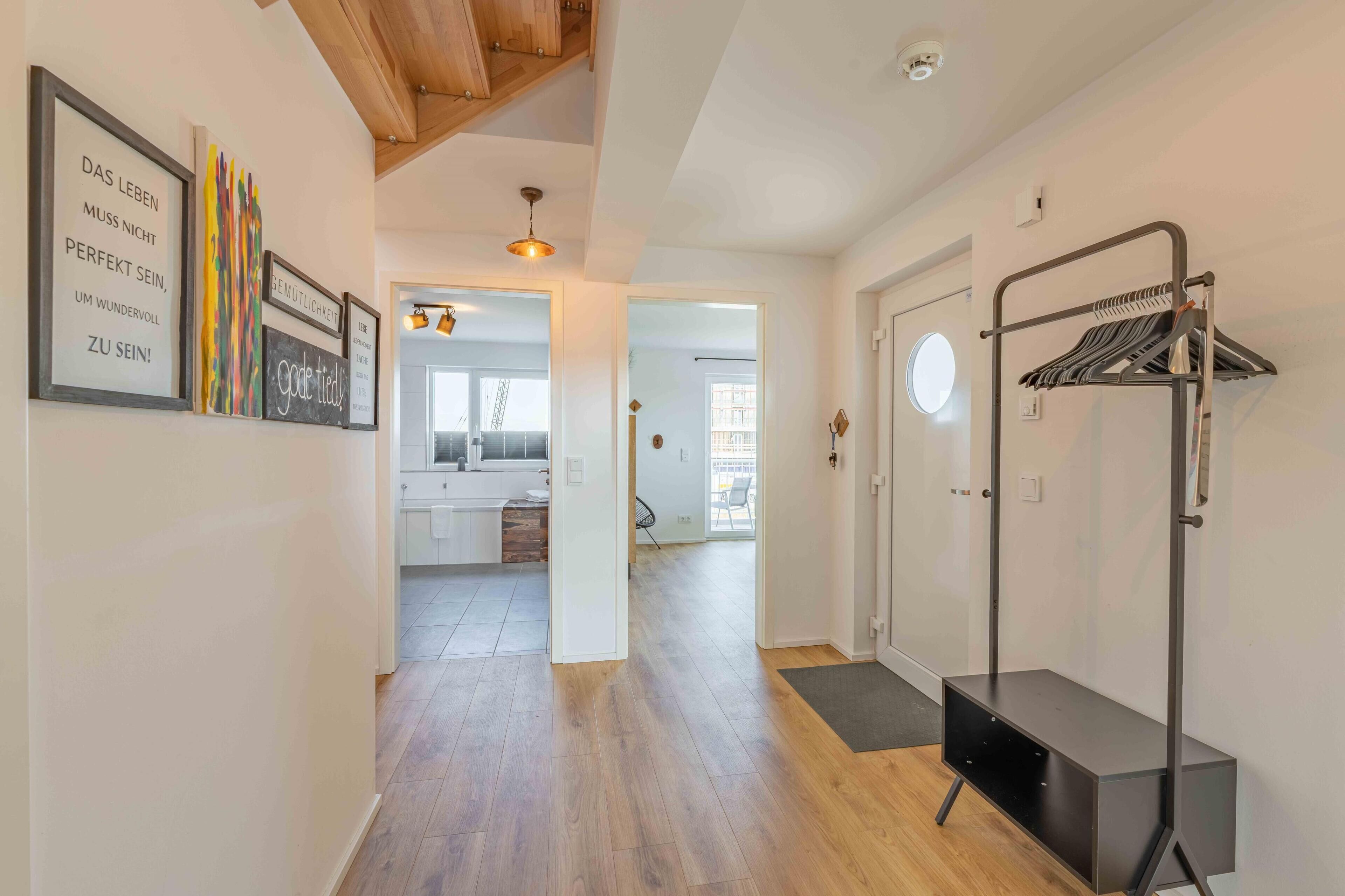 A hallway with wooden flooring, a coat rack, and framed artwork on the walls.