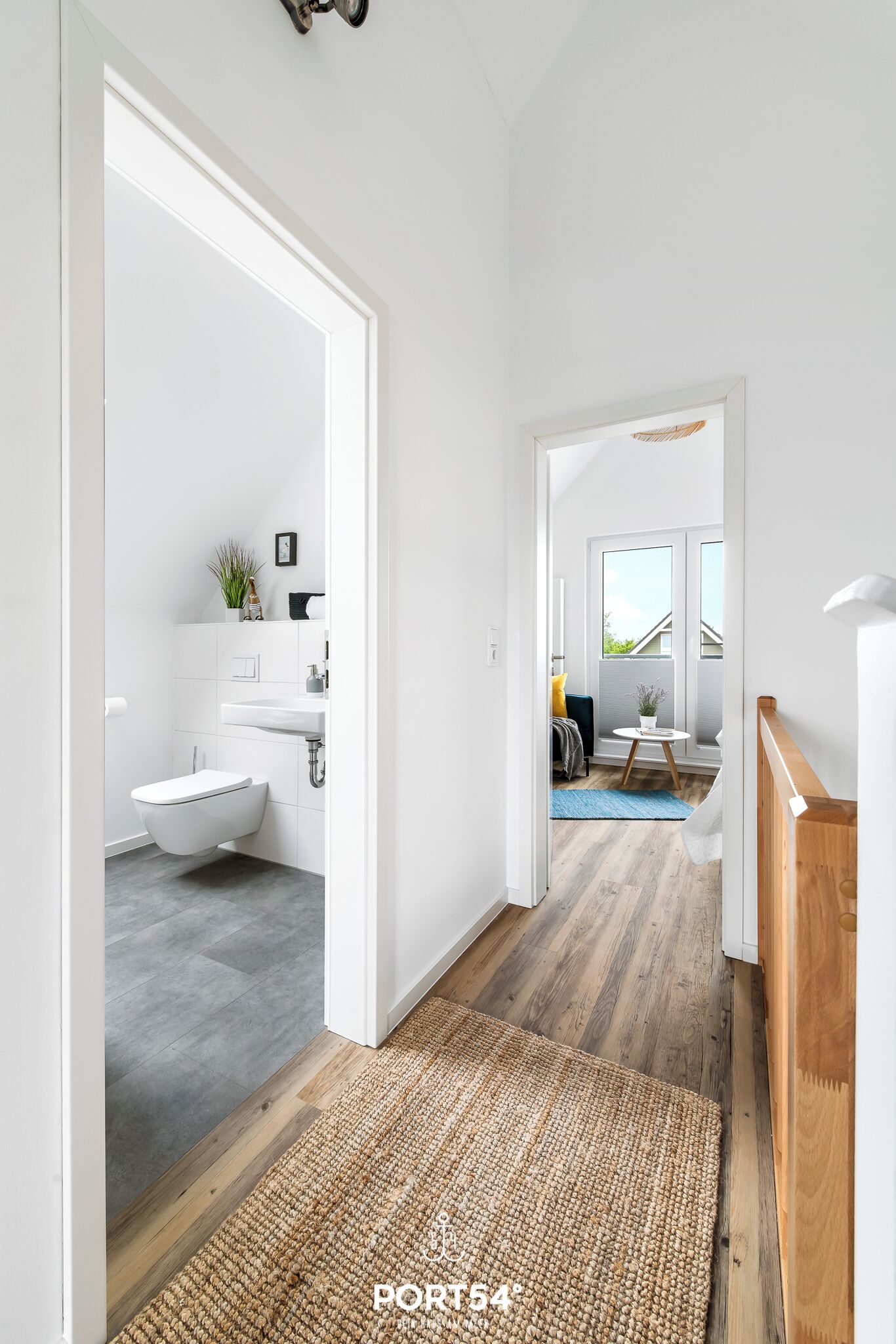 Een moderne, open woonkamer met een zichtbare badkamer, een houten vloer en uitzicht op een buitenruimte.
