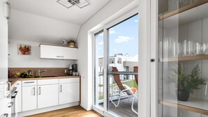 A modern kitchen with white cabinets, a wooden countertop, and a sliding glass door leading to a balcony with a chair and a potted plant. - Strandmuschel 65-Balcony, Infrared Sauna, Shower, Fireplace, EV Charging Station (Olpenitz)