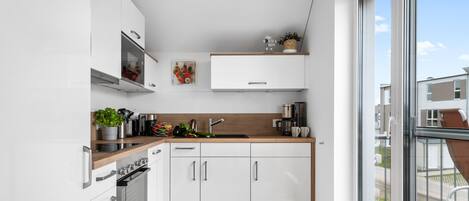 A modern kitchen with white cabinets, a wooden countertop, and a large window offering a view of the neighborhood.