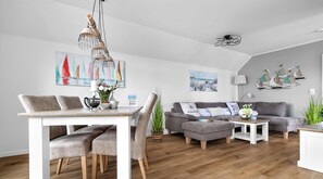 Una sala de estar moderna con comedor, sofás grises, una mesita de centro y una lámpara colgante.