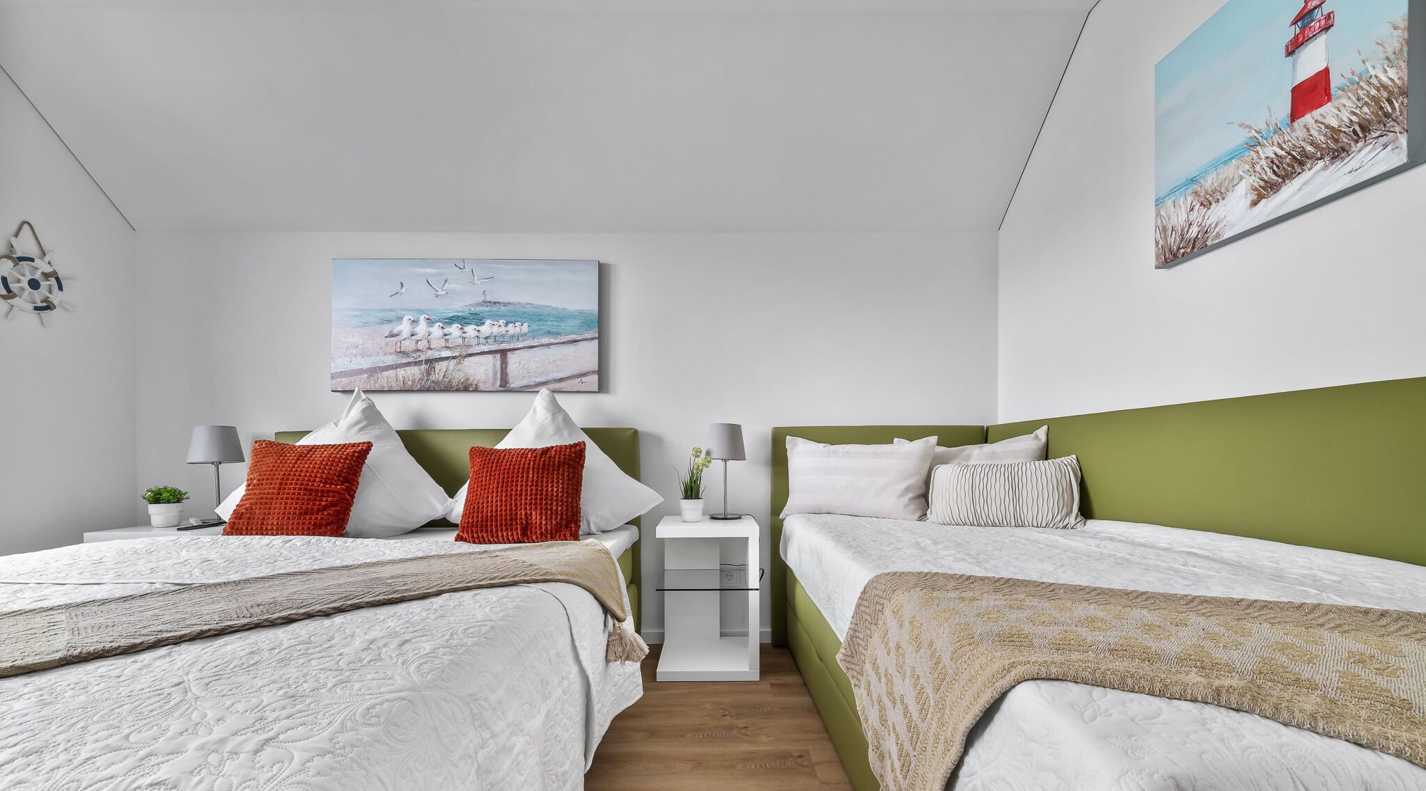A modern bedroom with two beds, a nightstand, a lamp, and a painting of a lighthouse.