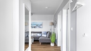 A modern living room with a grey sofa, a painting of a beach scene, and a potted plant. - Strandmuschel 65-Balcony, Infrared Sauna, Shower, Fireplace, EV Charging Station (Olpenitz)