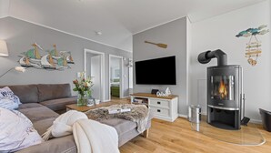 A modern living room with a sofa, a flat-screen TV, a fireplace, and decorative wall art. - Strandmuschel 65-Balcony, Infrared Sauna, Shower, Fireplace, EV Charging Station (Olpenitz)