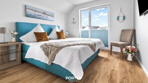 A bedroom with a bed, a nightstand, a chair, and a window with a view of the sea. - Strandmuschel 65-Balcony, Infrared Sauna, Shower, Fireplace, EV Charging Station (Olpenitz)