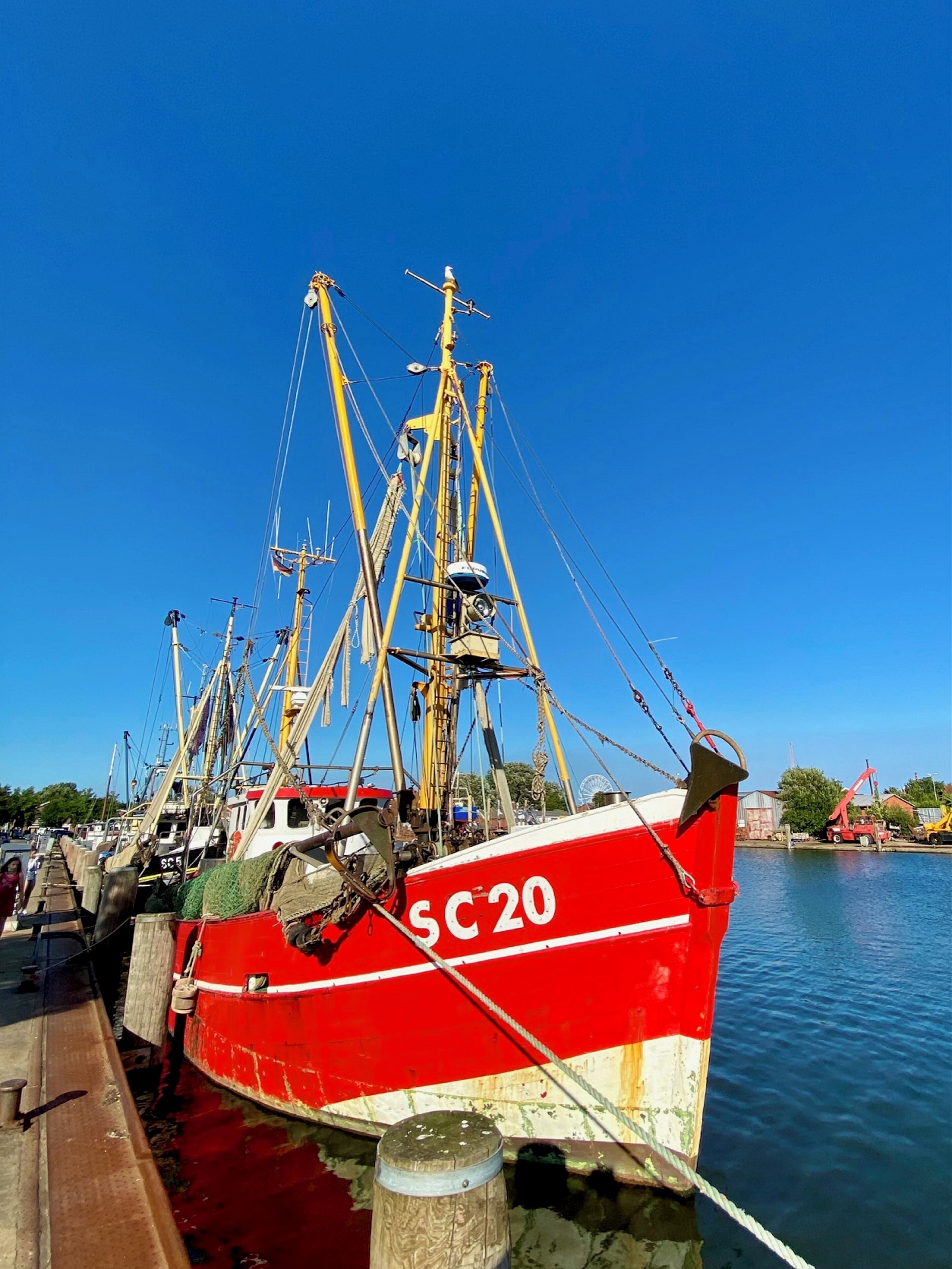 A red fishing boat docked at a pier with a clear blue sky in the background.