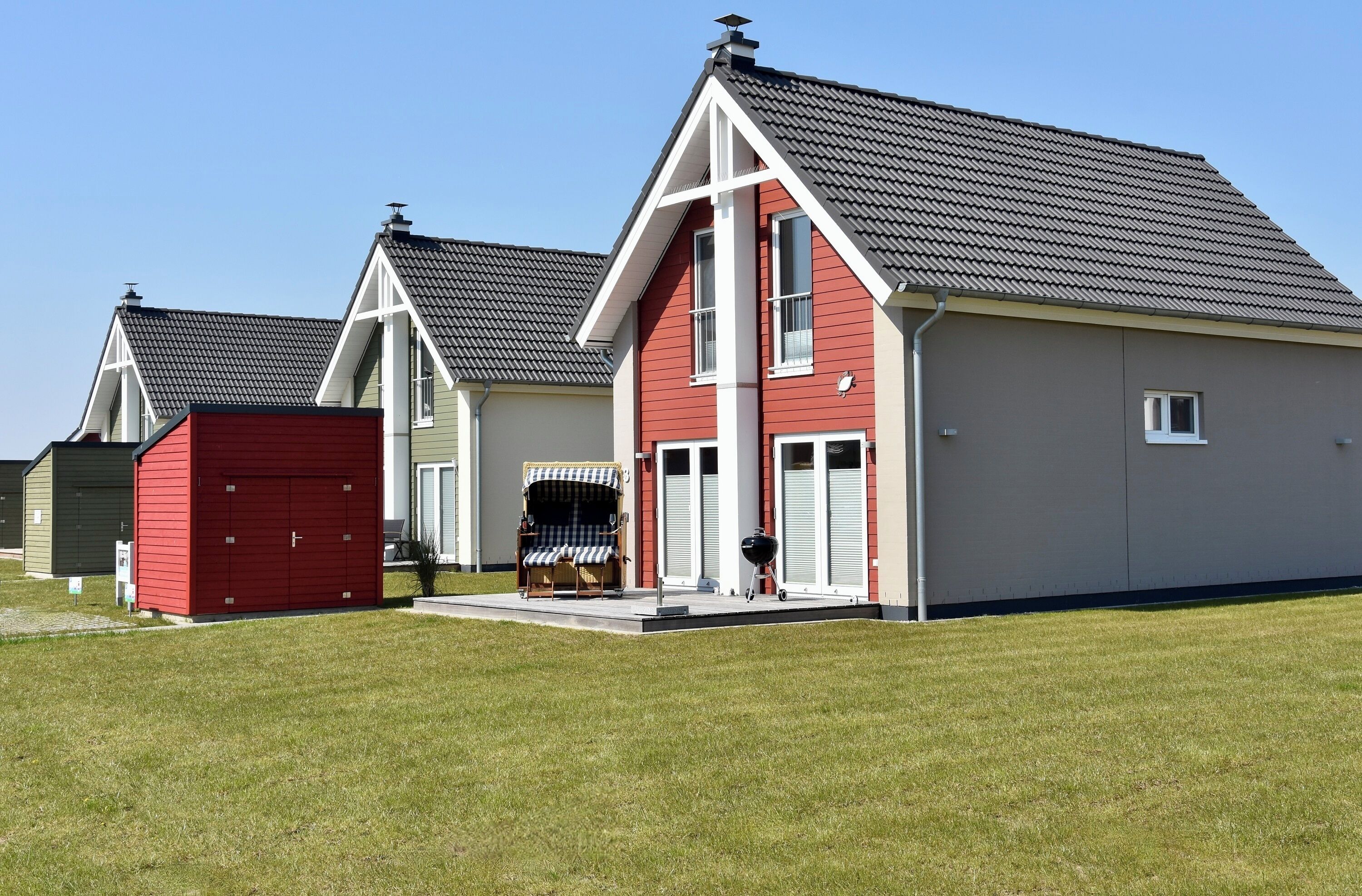 A row of modern houses with red and grey exteriors, each with a garage and a small porch area.