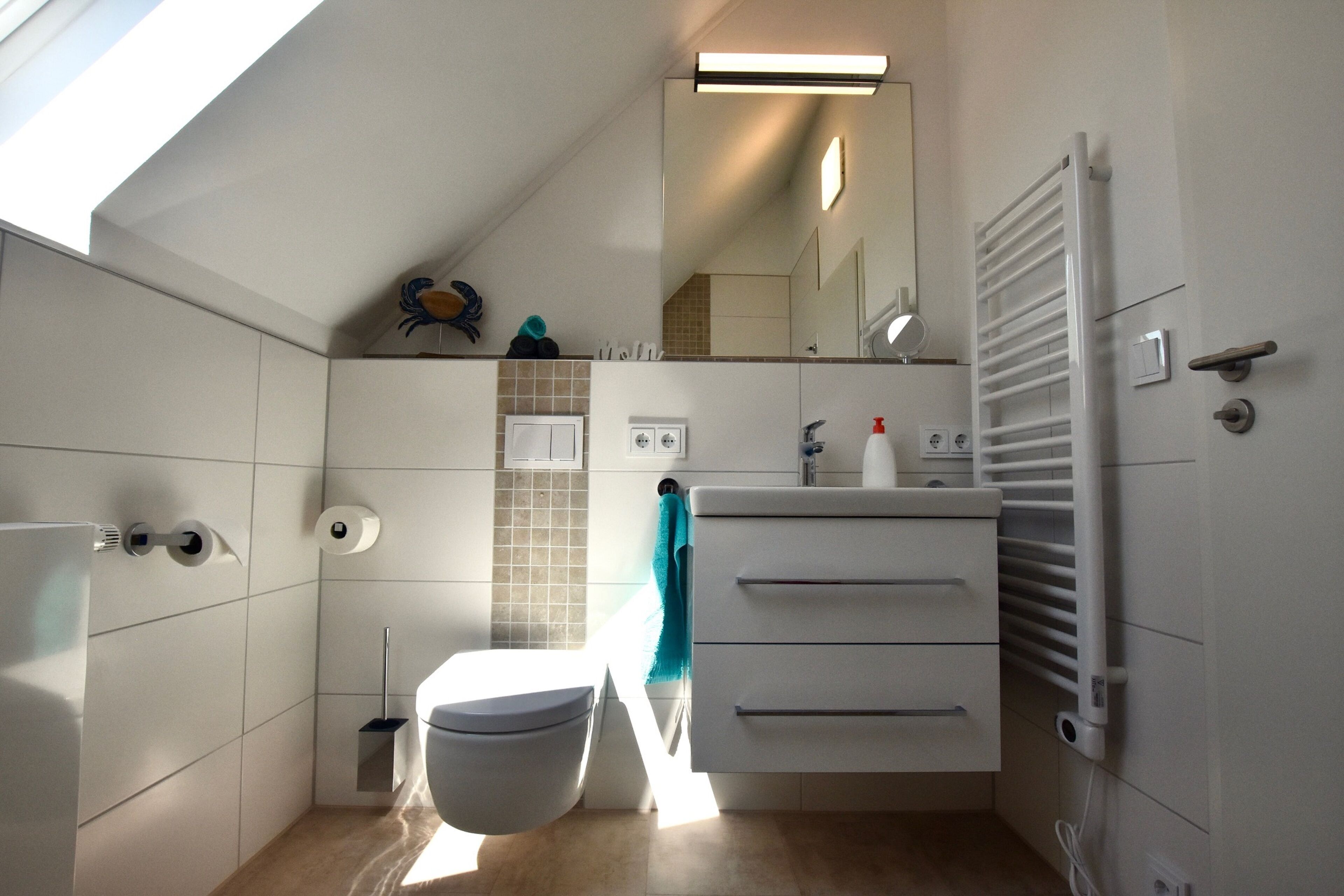 A modern bathroom with a skylight, white tiles, a toilet, a sink with a mirror, and a towel rack.