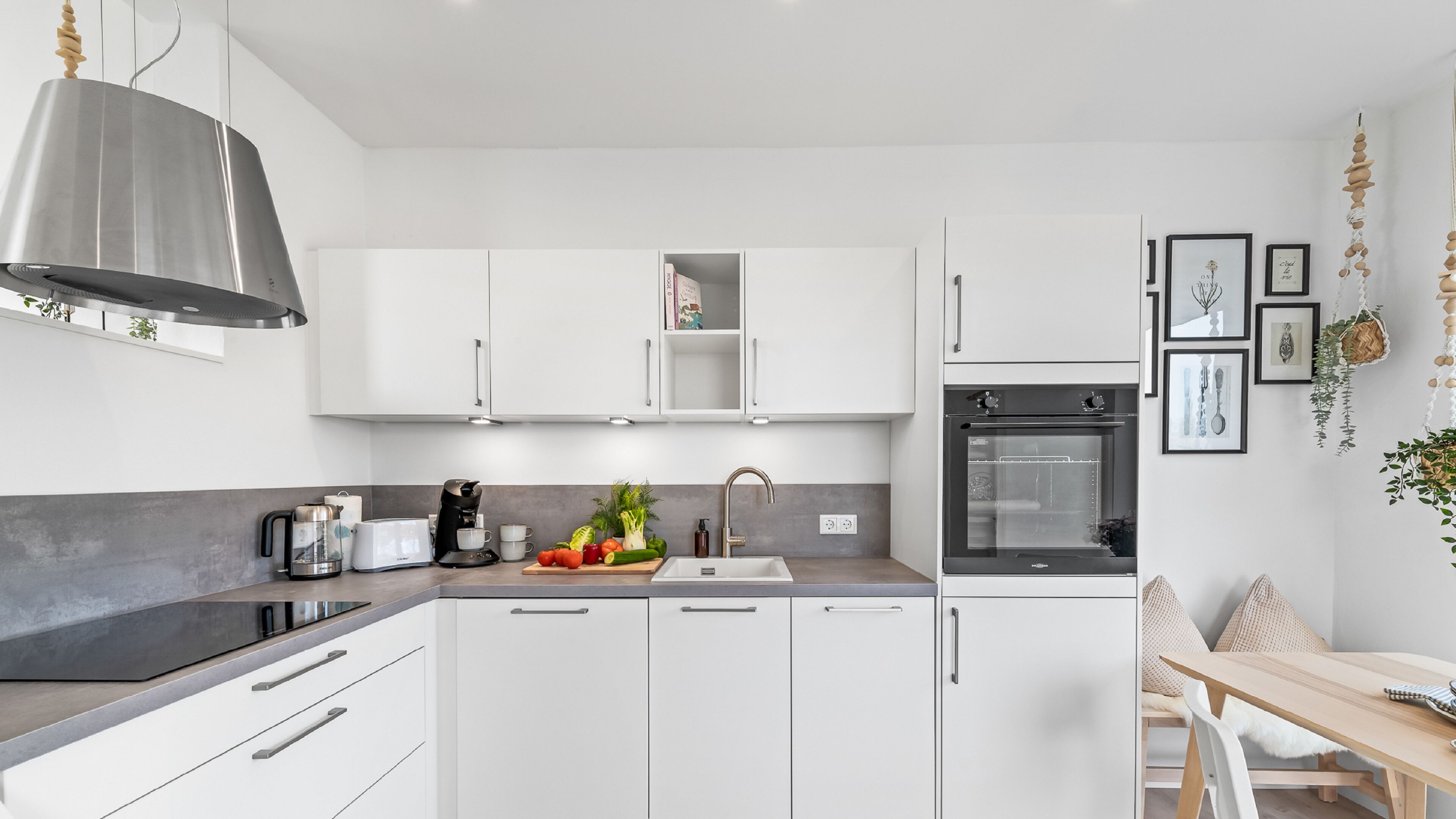 A modern kitchen with white cabinets, a built-in oven, and a dining area with a wooden table and chairs.
