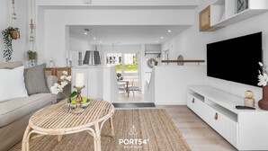 A modern living room with a sofa, a dining table, and a TV. There is a kitchen in the background. - Meerliebe – sea view, roof terrace, infrared sauna, shower, EV charging station (Glücksburg)