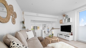 A modern living room with a beige sofa, a flat-screen TV, and a large window. - Meerliebe – sea view, roof terrace, infrared sauna, shower, EV charging station (Glücksburg)