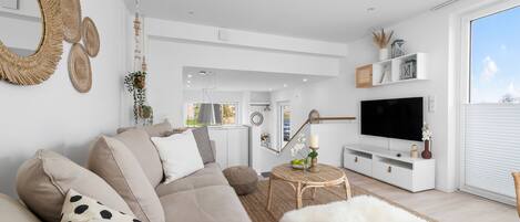 A modern living room with a beige sofa, a flat-screen TV, and a large window.
