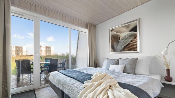 Ein Schlafzimmer mit einem großen Bett, Blick ins Freie und einem gerahmten Bild an der Wand.
