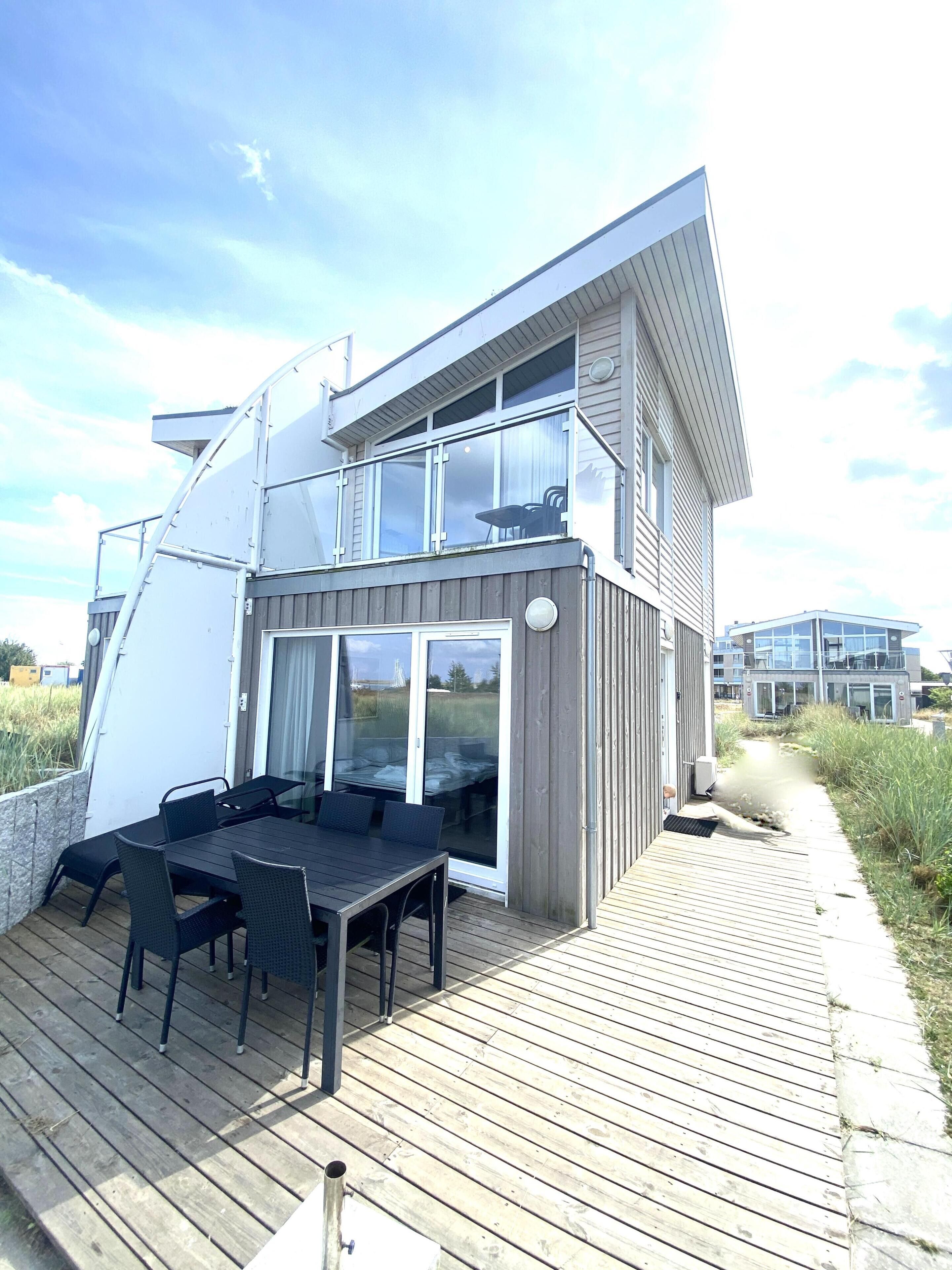 A modern house with a deck, large windows, and a view of the sea.